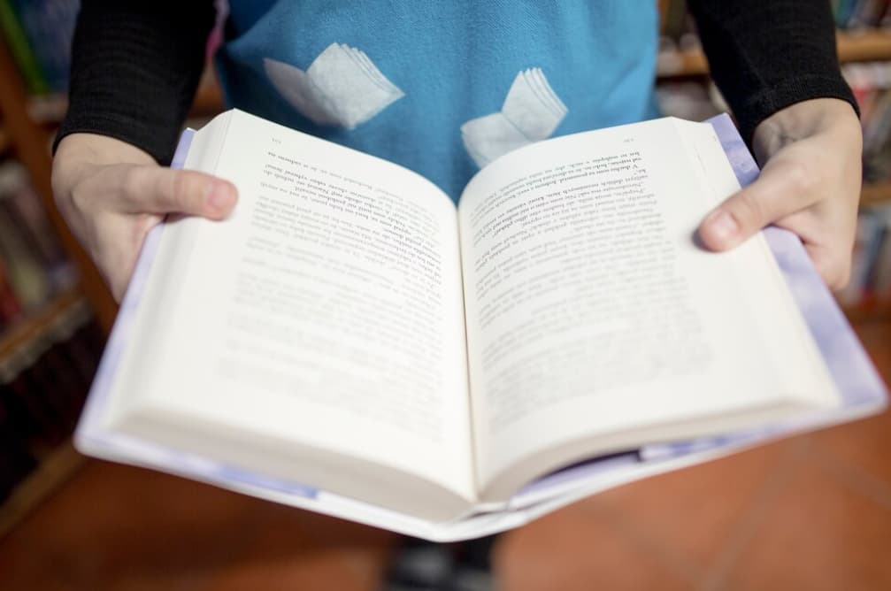 Person in a blue sweater holding an open book