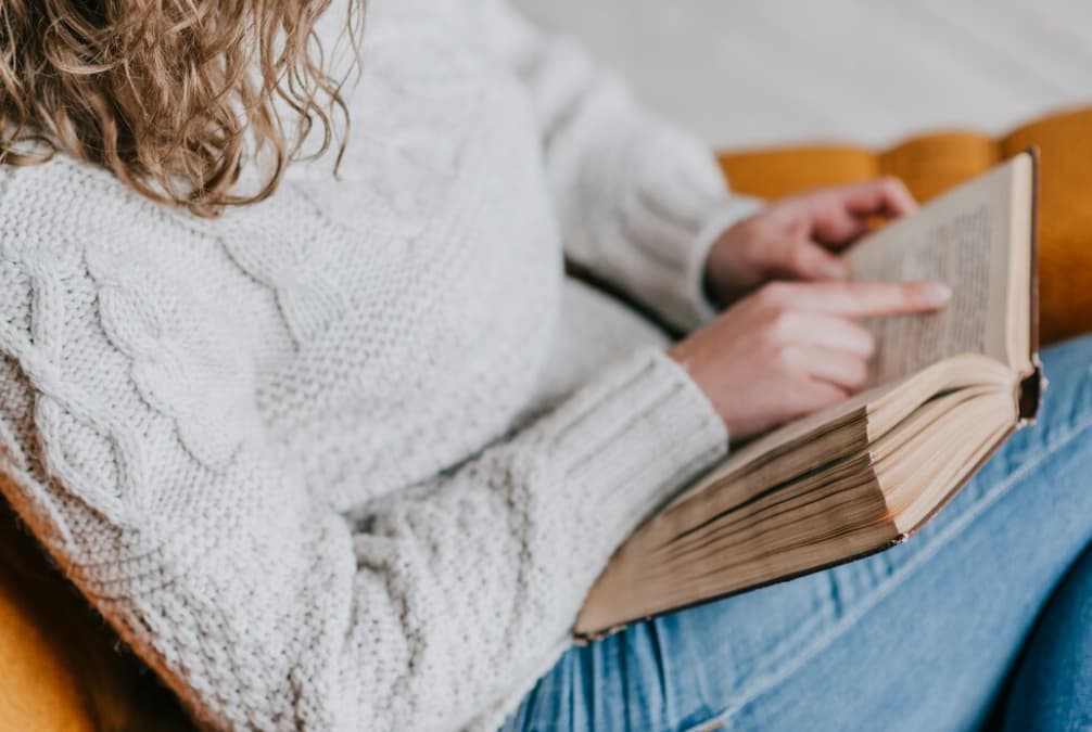 Close-up of a person in a sweater reading an old book