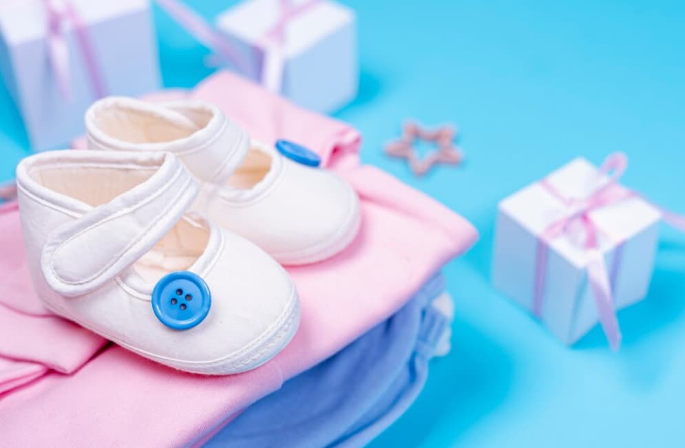 White baby shoes on pink fabric with gift boxes behind