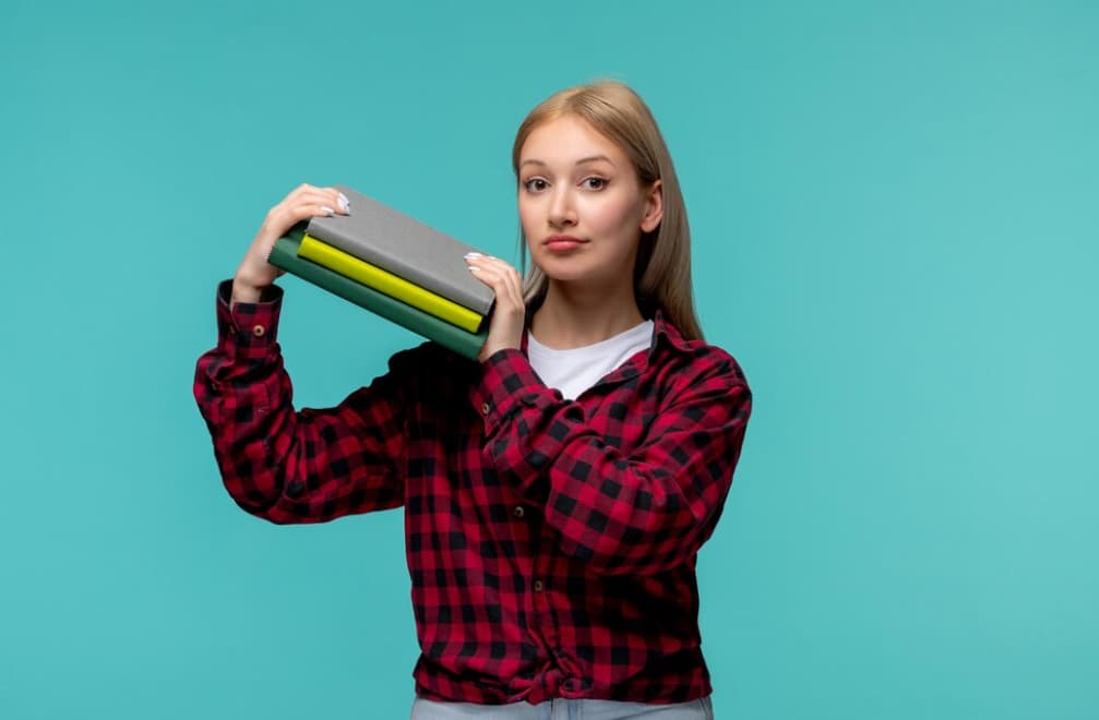 A young woman holds textbooks and poses confidently on a teal background