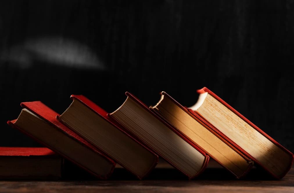 Red-bound books lean on each other, forming an arch