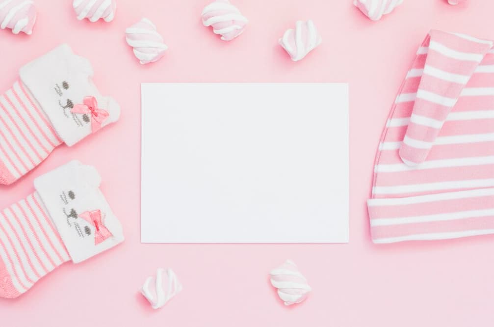 Pink baby socks and blank card with marshmallows on a pink backdrop