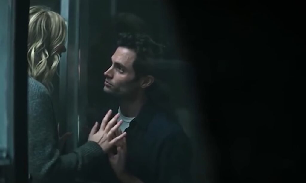 Two people touching hands through a glass partition